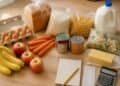 Weekly groceries for a family arranged on a kitchen counter next to a handwritten shopping list, a receipt and a calculator